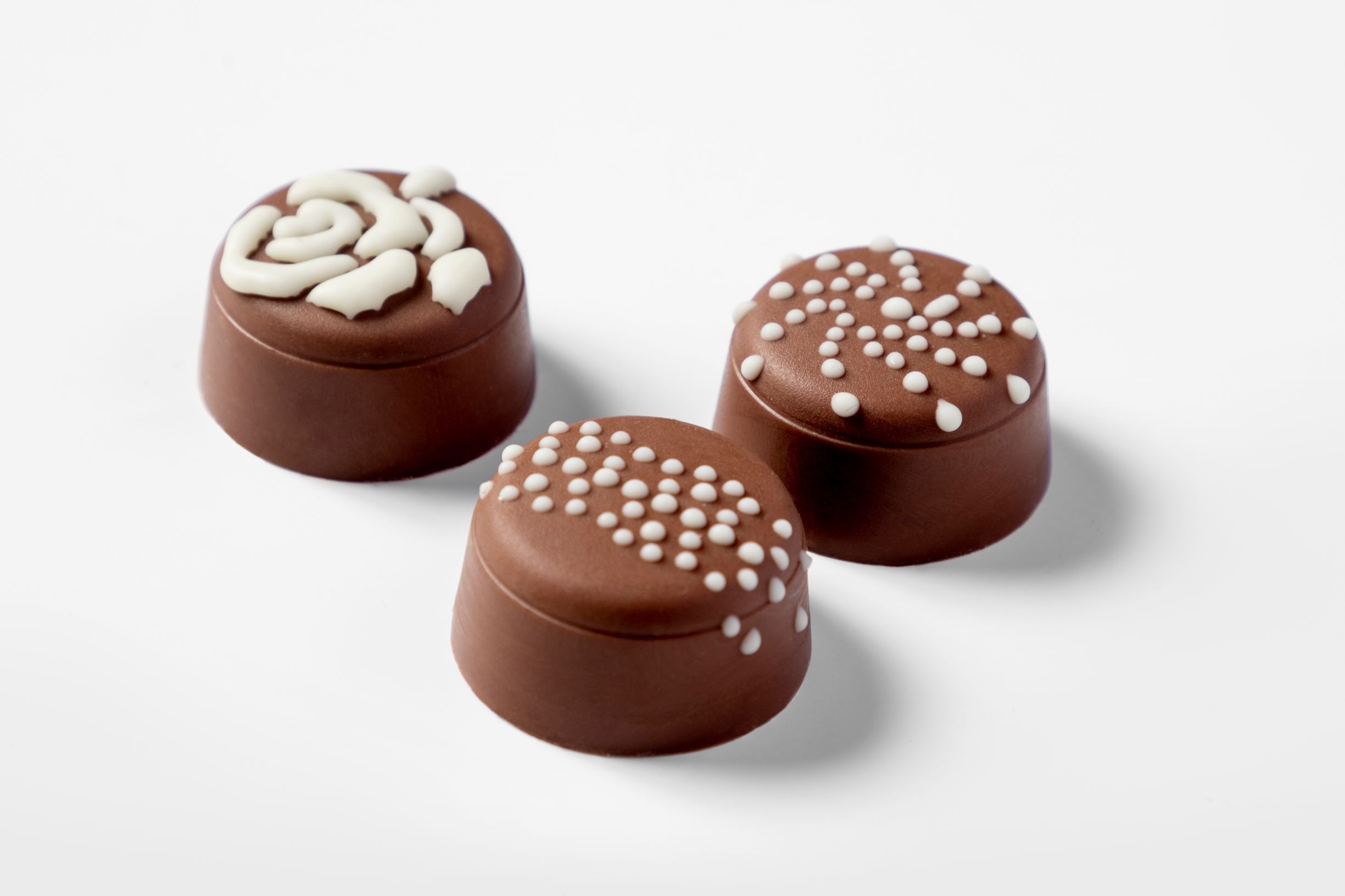 Three milk chocolate pralines decorated with white chocolate by a FoodJet precision depositing system