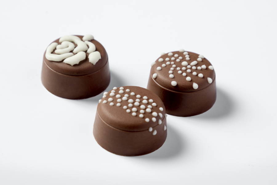 Three milk chocolate pralines decorated with white chocolate by a FoodJet precision depositing system