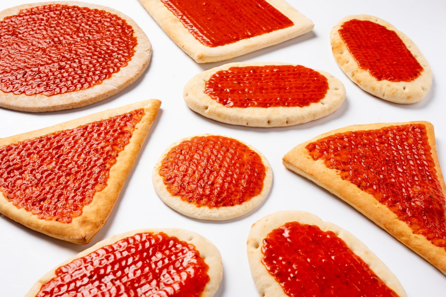 Various slices of pizza in different shapes covered by FoodJet pizza sauce depositor