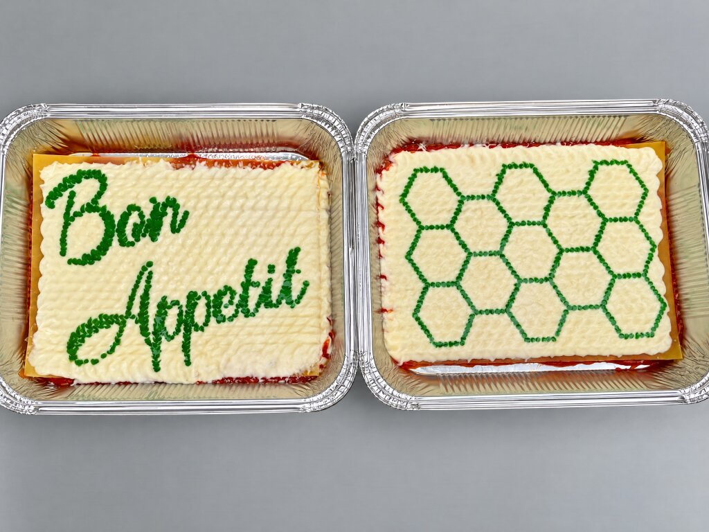 Two lasagne trays with bechamel decorated in green dots: the words Bon Appetit and a honeycomb
