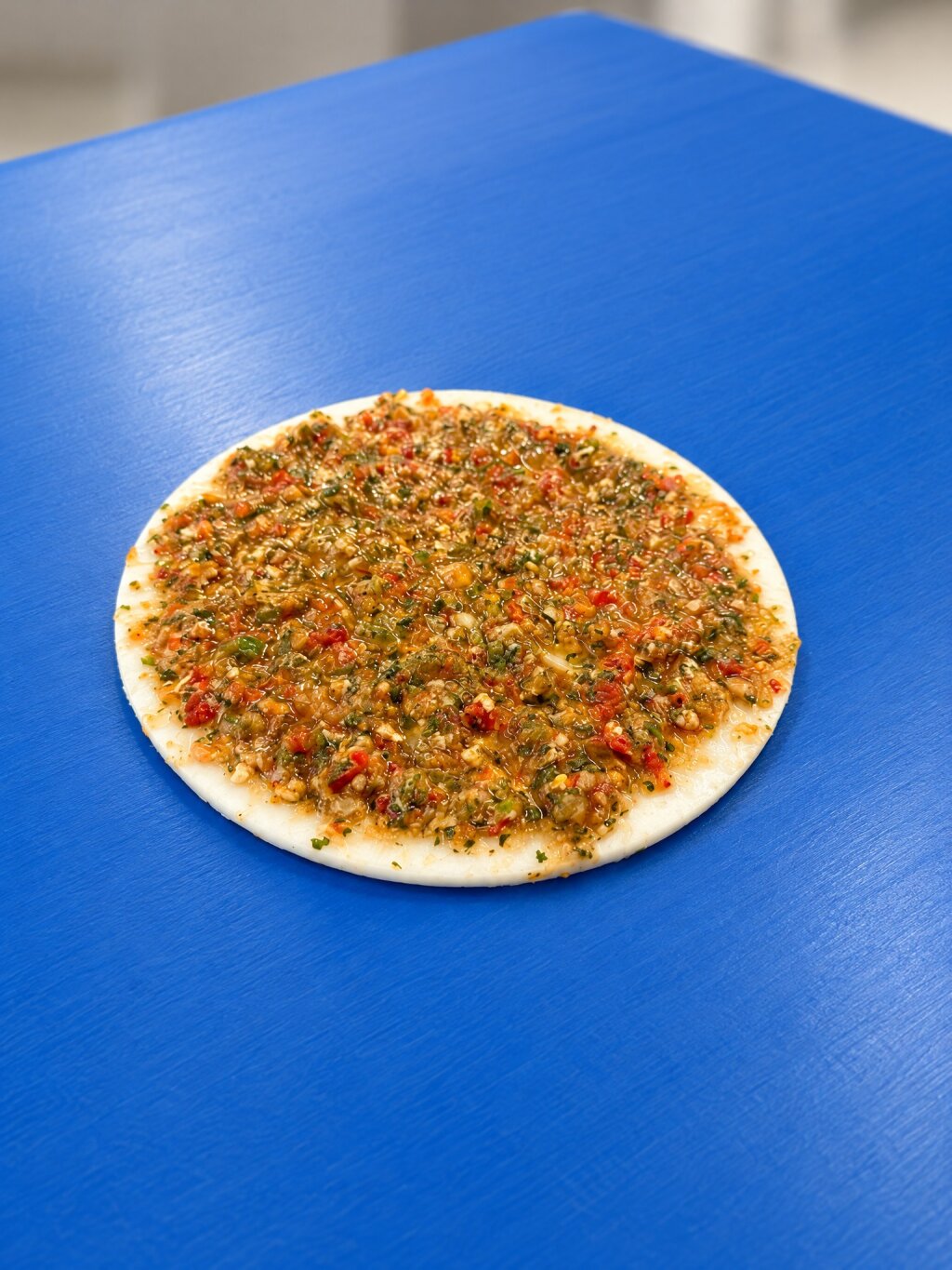 Round white carrier disc covered with a coarse vegetable and tomato topping, on a blue belt