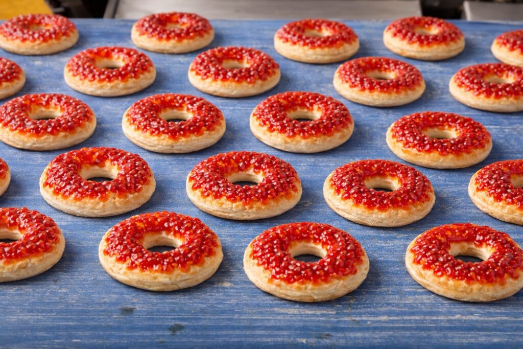 Donut-shaped mini pizzas with tomato sauce deposited in drops, on a blue conveyor