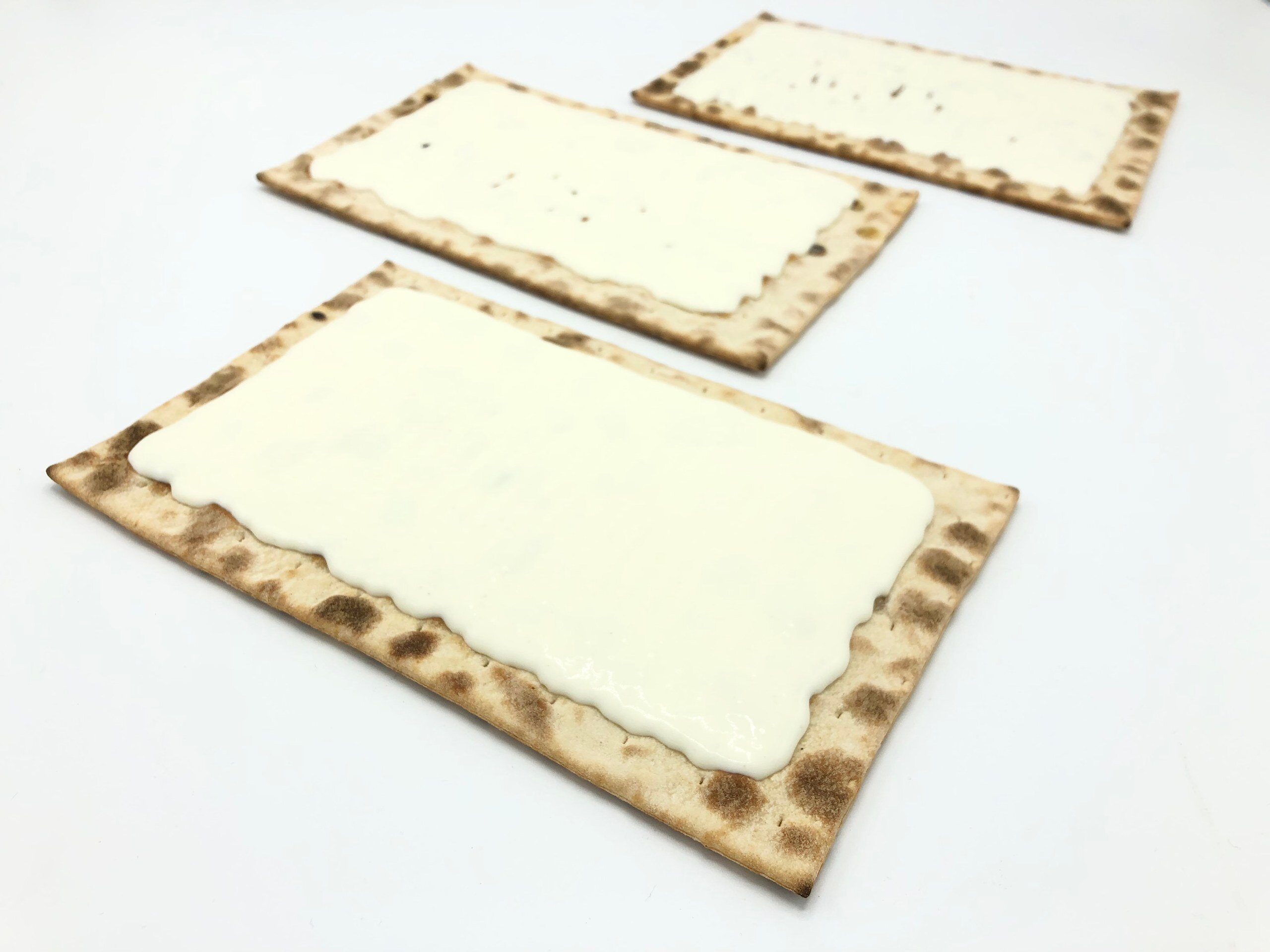 Three rectangular flammkuchen bases with a layer of crème fraîche on top, on a white surface