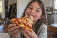 Cheerful girl taking a bite of a pizza slice with tomato sauce and stretching melted cheese
