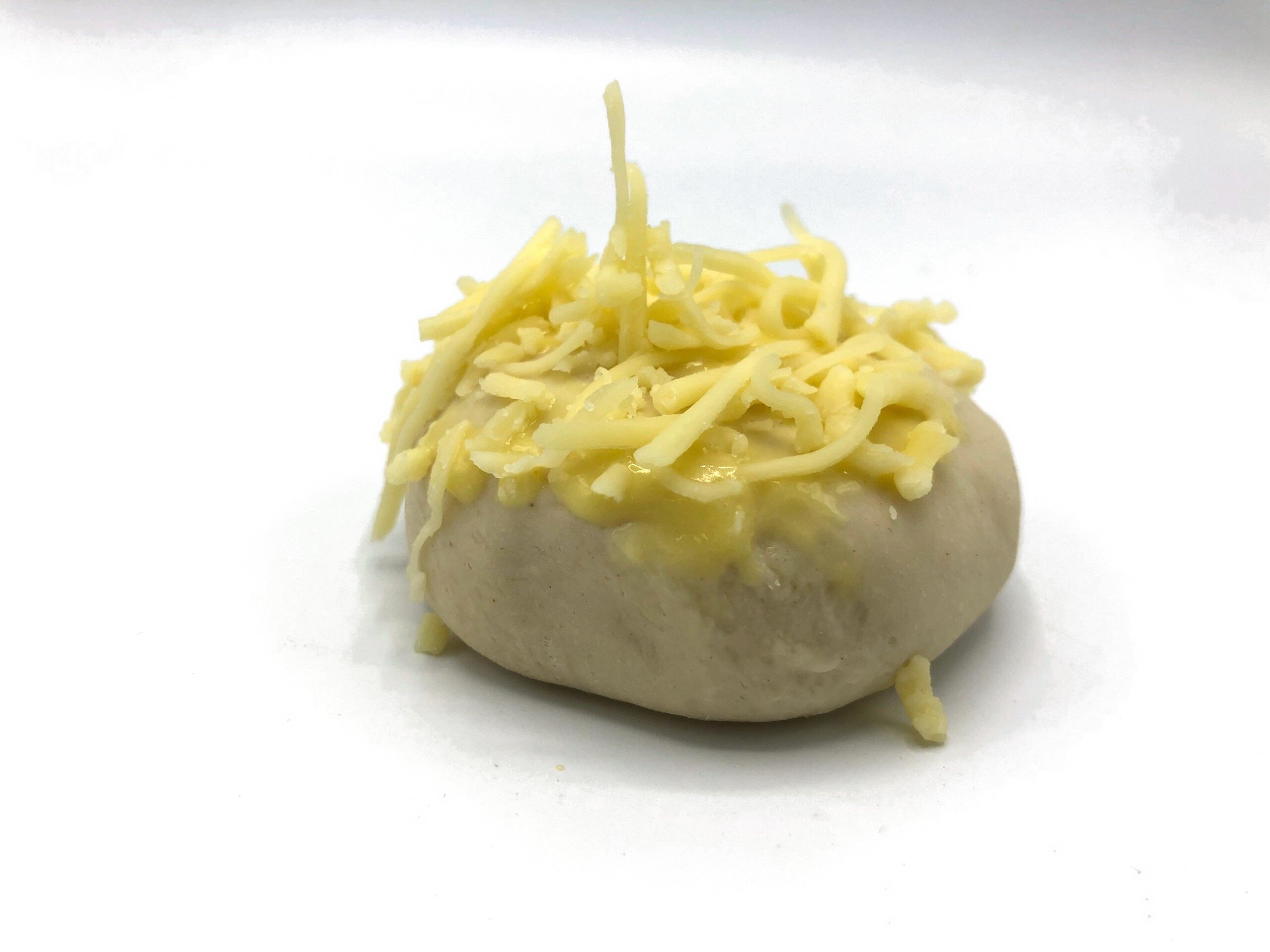 Dough ball topped with a deposited cheese sauce and grated cheese