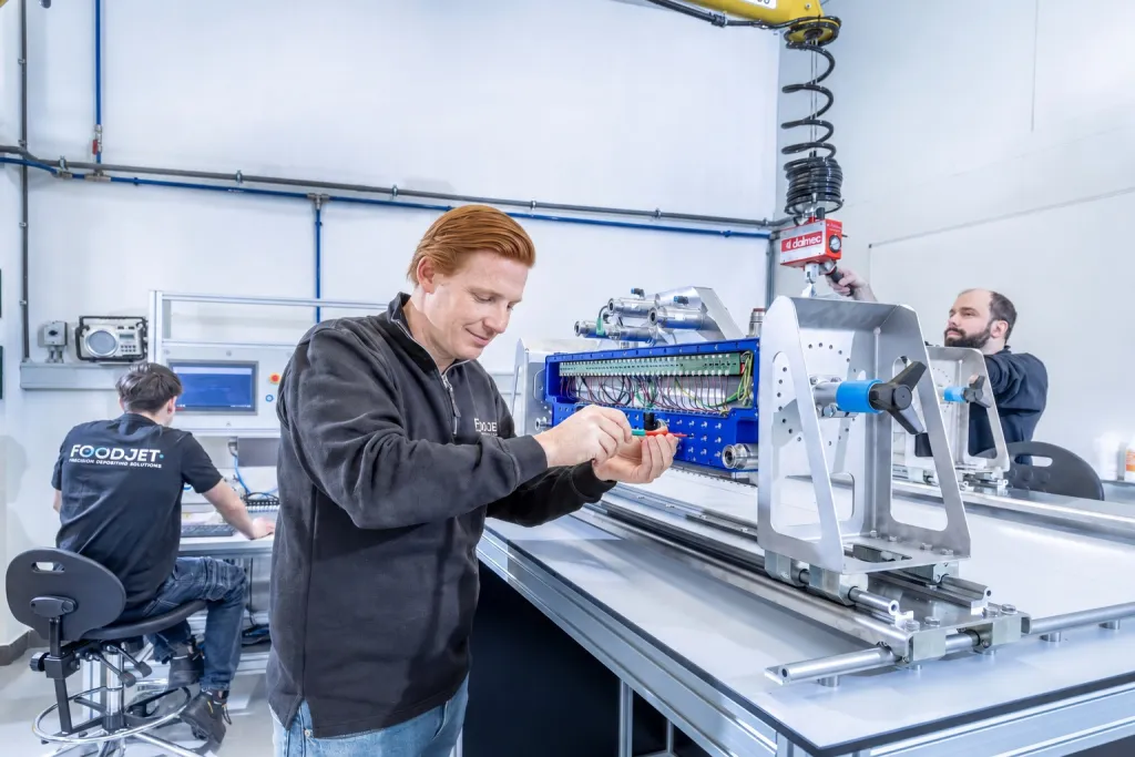 Technician looking at a depositing head while assembling it, with colleagues at work in the background